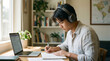 © Vera D - Focused young asian man in headphones studying on laptop computer at desk, writing notes in notebook, male university student listening to webinar or e-learning podcast in home office interior