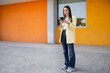 © ADDICTIVE STOCK - Young woman using smartphone against colorful wall outdoors