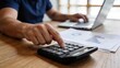© Noah - Businessman calculating financial data with calculator and laptop, analyzing charts and graphs on desk, corporate accounting concept.