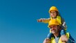 © WindyNight - Caucasian construction dad in yellow hard hat carrying his young son on shoulders at building site. Son is pointing excitedly. Both smiling at camera. Father's Day builder family concept, copy space.