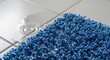 © Nataly - Blue bath rug on tiled floor with water puddles highlighting the absorbent fibers and textured surface. Bath rug provides comfort and style for bathroom spaces.