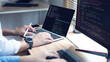 © Thanadon88 - Coder types on laptop with keyboard and monitor nearby. Hands rest on keys while stylus hovers above screen. Code lines glow in darkened workspace. Fingers move purposefully as programmer focuses
