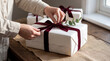 © Rendara Studio - Hands tying velvet ribbon on wrapped Christmas gift by window