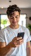 © subur - Smiling Young Man Looking at Smartphone Indoors in Casual White Shirt