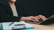 © Mdisk - Professional businesswoman wearing black formal blazer types laptop keyboard beside clipboard pen credit card nearby against dark background indoors evening office work session performing financial.