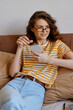 © SHOTPRIME STUDIO - Young woman at home relaxing on a sofa, using a smartphone, wearing striped t shirt and glasses, casual lifestyle scene with natural light and cozy decor. Soft background music implied.