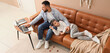 © Pixel-Shot - Happy father using laptop while his son sleeping on brown leather sofa at home