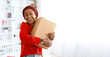 © Prostock-studio - A young woman stands in her living room, holding a large cardboard package close to her body. She has a big smile on her face as she enjoys the moment. Bright light enters from the window