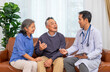 © Verin - A male doctor or caregiver measuring mercury and explaining a senior man on sofa, with his supportive wife sitting beside during a home medical visit