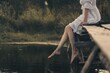 © junky_jess - Atmospheric scene of faceless young woman in white vintage dress sitting and swinging her bare legs on old wooden pier over dark wild pond in summer