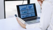 © Phushutter - Businesswoman reviewing financial charts on a laptop while holding a smartphone at a desk in a bright office. Ideal for business analysis, reporting, technology, and remote work themes.
