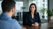 © Nuttawut - Serious Business Discussion: A focused woman in a dark suit engages in an intense discussion with a colleague across a polished wooden table in a modern office.