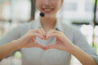 © MINAE - Call center employee wearing headset forming an adorable heart shape with hands, showing care and excellent customer service with a friendly smiling face