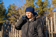 © Анастасия Бурлакова - Man wearing winter clothes talking on a mobile phone outdoors. Casual young guy using smartphone for a conversation in nature. Cold weather communication and technology connectivity concept.