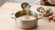 © Wankatsu - Pouring clear bone broth from a ladle into a stainless steel pot with marrow bones and shallots on a wooden table culinary cooking lifestyle concept
