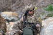 © Supachai - Soldier in camouflage uniform talking on tactical military radio transceiver station outdoor, special forces operator using communication equipment near rock cliff background