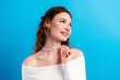 © deagreez - Smiling young woman wearing a pearl necklace and off-shoulder sweater against a bright blue background