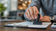© RA_DESINER - A man's hand stamping a document with a black rubber stamp on a wooden desk.