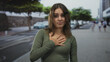 © Krakenimages.com - Young woman with hand on chest wearing green shirt and necklace on city street pedestrian walkway; regret apology.