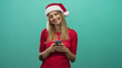 © Krakenimages.com - Blonde woman smiling while typing on smartphone with thumbs, wearing santa hat and red top in studio; festive contentment.