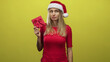 © Krakenimages.com - Woman holding red gift, touching santa hat and pursing lips against yellow studio backdrop; holiday skepticism.