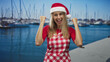 © Krakenimages.com - Woman wearing santa hat and checkered apron pumps fist on marina dock beside sailboats while smiling broadly; holiday joy.