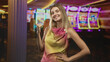 © Krakenimages.com - Woman smiling with fist pump and hand on hip, wearing colorful sleeveless dress, standing before slot machines in casino; joy confidence.
