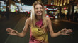 © Krakenimages.com - Blonde woman smiling and dancing with raised hands near a red double decker bus in a night city street; joyful.