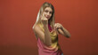 © Krakenimages.com - Woman with raised fists and visible forearms in a studio, mock boxing pose with direct gaze, wearing a sleeveless pink and yellow top; playful challenge.
