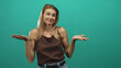 © Krakenimages.com - Woman shrugs with palms up and bare forearms visible in a teal studio, blonde young caucasian wearing brown sleeveless top and jeans belt; uncertainty humor.