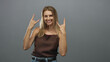 © Krakenimages.com - Blonde woman wearing brown top and jeans, hands forming rock horns while smiling against a grey studio backdrop; playful confidence.