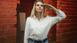 © Krakenimages.com - Woman salutes with hand to forehead in a brick building interior wearing white shirt and jeans, facing camera; confidence duty respect.
