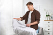© New Africa - Man ironing curtain on board at home