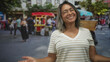 © Krakenimages.com - Middle age hispanic woman smiling with open hands near a food cart on a busy street market, wearing glasses and a striped shirt; joy warmth.