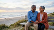 © Xenia - Happy elderly diverse couple holding hands on a beach bench. Smiling senior man and woman enjoying a romantic sunset by the ocean. Retirement travel and vacation concept