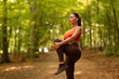 © Home-stock - Woman warming up, standing on path in forest, stretching her legs while preparing for workout in early morning light, copy space