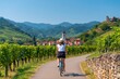 © oksa_studio - Cycling woman on bicycle through lush alsace vineyard in france summer travel