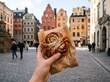 © FOODS and TRAVEL - A hand holding a Swedish cinnamon bun on a historic city square