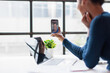 © David - Woman working remotely, holding a smartphone during a video call, communicating with a colleague on screen, embracing modern remote work and virtual connection while staying productive
