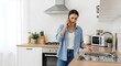 © pika - Young woman talking on phone in modern kitchen, looking at sink, possibly dealing with a plumbing issue or home repair.