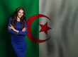© millaf (Nemchinova) - Successful young woman in blue dress smiling against flag of Algeria background