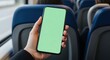© Syafiq Rahman - A person holds a smartphone with a vibrant green screen displaying an advertisement or application interface while traveling seated within a public transportation vehicle, likely a bus or train
