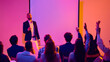 © Lustre Art Group  - Male speaker answering audience questions beside blank screen in neon seminar room. Concept of Q and A session, business workshop, leadership training, public speaking and corporate education.