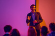 © Lustre Art Group  - Smiling businessman leading seminar discussion in neon lit meeting room. Concept of leadership workshop, corporate learning, motivational speech, audience engagement and business education.