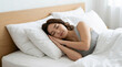 © jack - Young woman sleeping peacefully in a comfortable bed with white pillows and bedding in a bright minimalist bedroom during daytime
