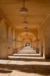 © Val MAK - Sunlit arched corridor with repeating columns and patterned shadows