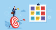 © Soriful - Businessman standing on giant target next to board with colorful sticky notes for project management and goal achievement.