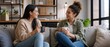 © Vasiliy - Two young women talking and drinking coffee on a sofa. Friends having a conversation in a modern living room. Lifestyle and friendship concept