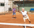 © JackF - Sporty aged family during doubles match on indoor tennis court. Active lady hitting tennis ball with racket