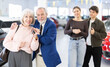 © JackF - Elderly is happy to buy a car, they are standing in a car dealership. Young gave their elderly parents a new car